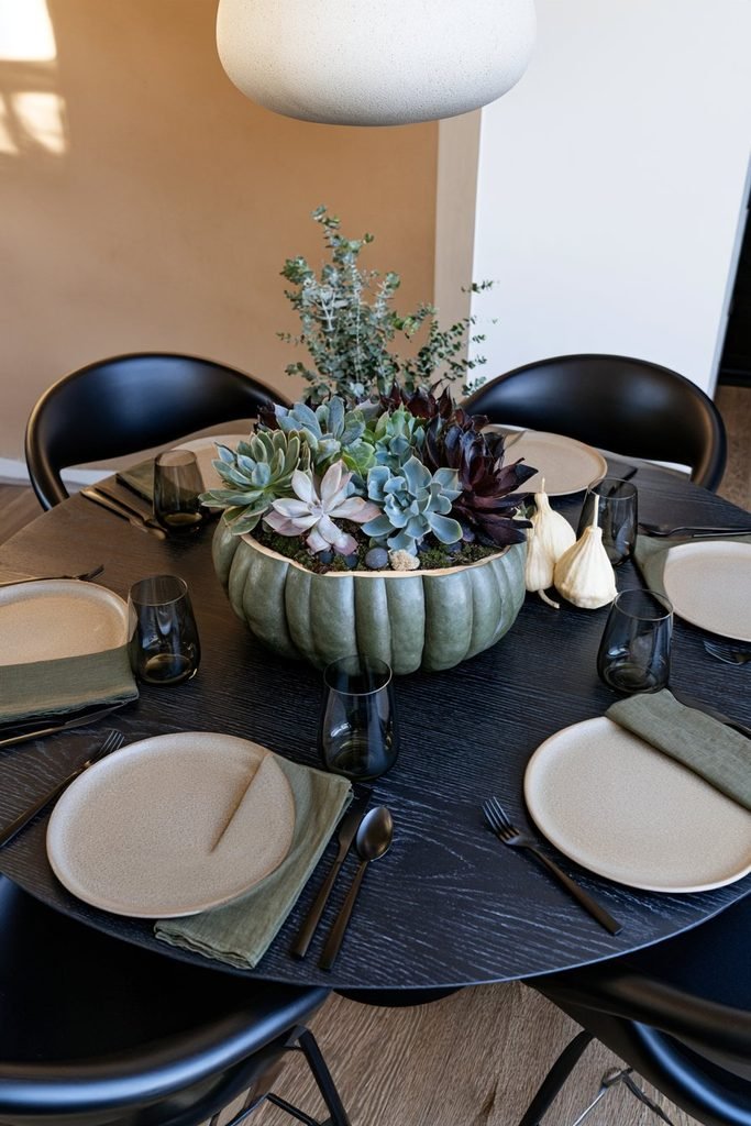 Modern Thanksgiving centerpiece featuring a sage-green pumpkin planted with living succulents, decorative moss, and natural stones.