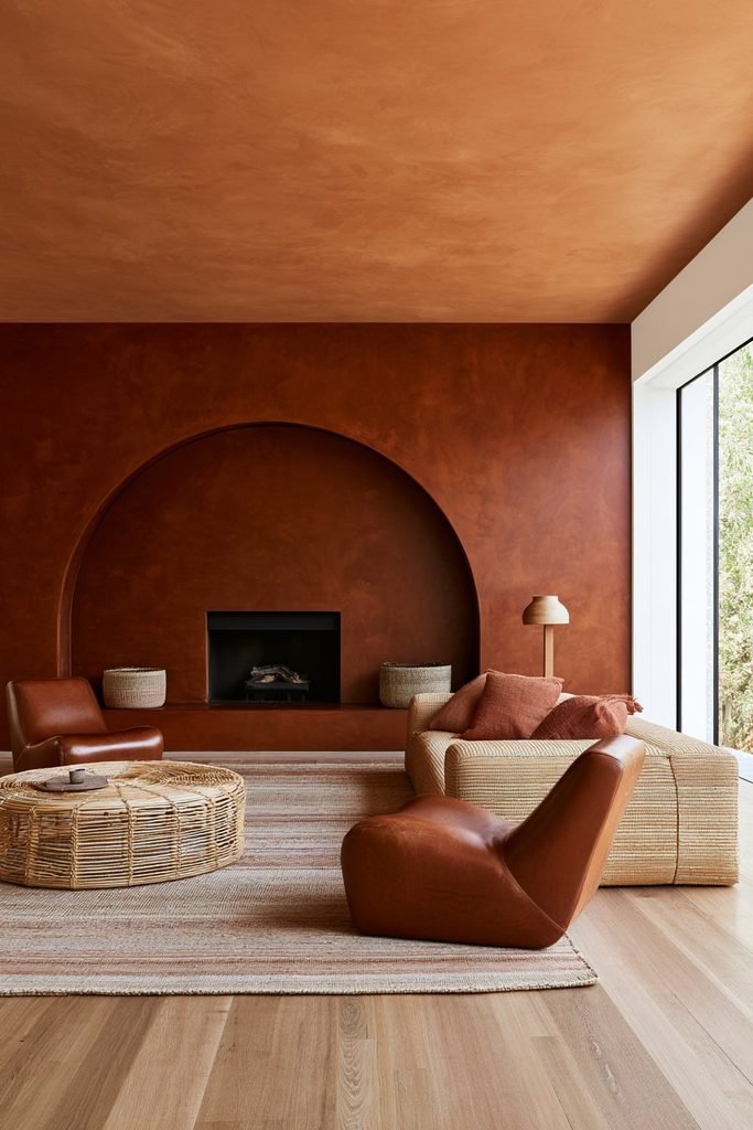 Warm terracotta colour-drenched living room with natural wood flooring, leather chairs and woven textures