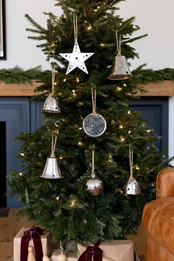 DIY metallic Christmas ornaments cut from recycled tin tubes and hung with jute twine on a naturally decorated evergreen tree.