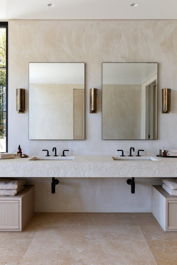 Taupe Venetian plaster bathroom vanity wall with a double oak vanity, brass sconces, and limestone countertop